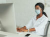 mulher com máscara trabalhando sentada em frente ao computador. Tempo de transmissão da covid mudou